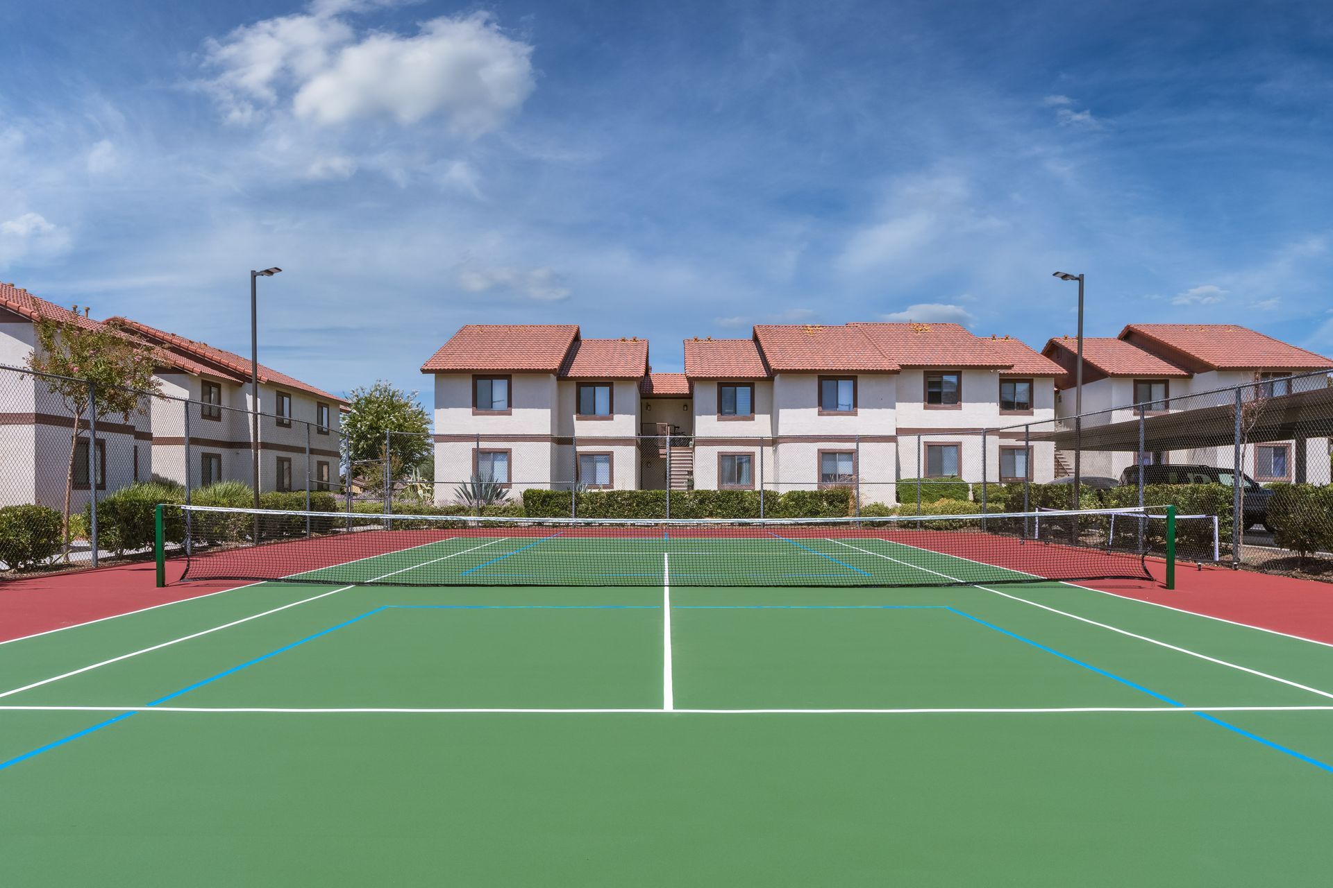 Tennis court with net, in front of apartment buildings on a sunny day.