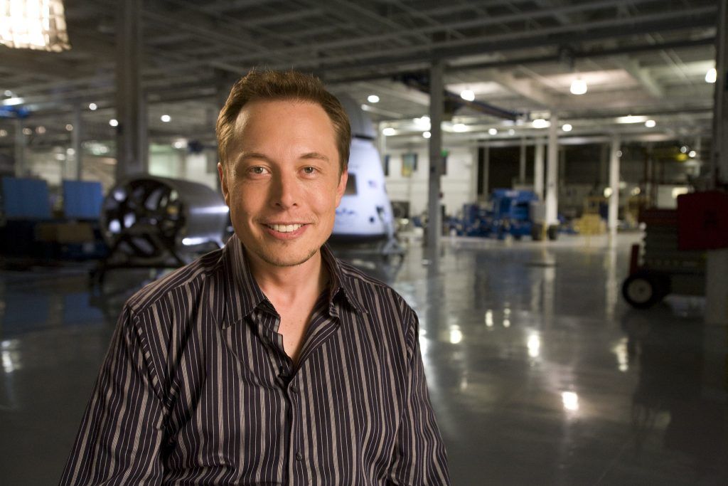 Person smiling in a large industrial warehouse with machinery in the background.