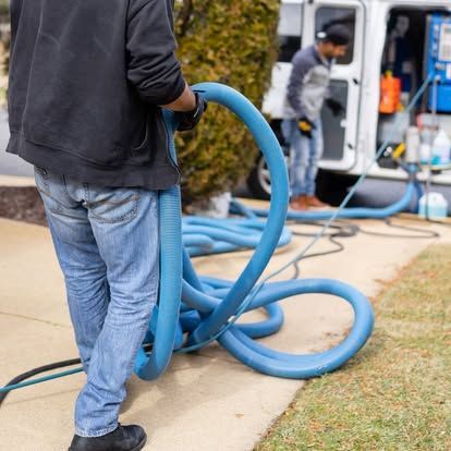 A man is holding a blue hose in front of a van.