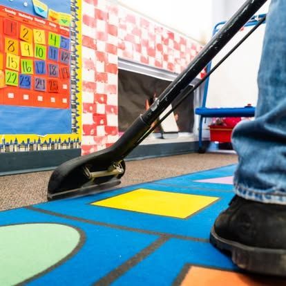 A person is using a vacuum cleaner to clean a colorful rug
