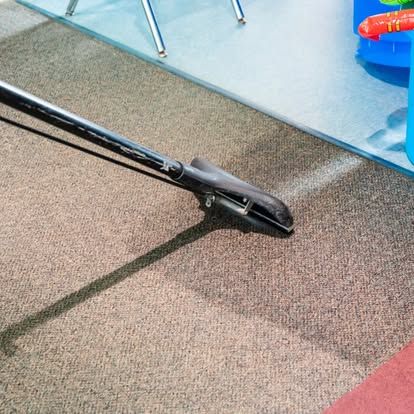 A vacuum cleaner is cleaning a carpet in a living room.