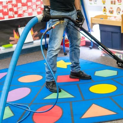 A man is cleaning a colorful rug with a vacuum cleaner.