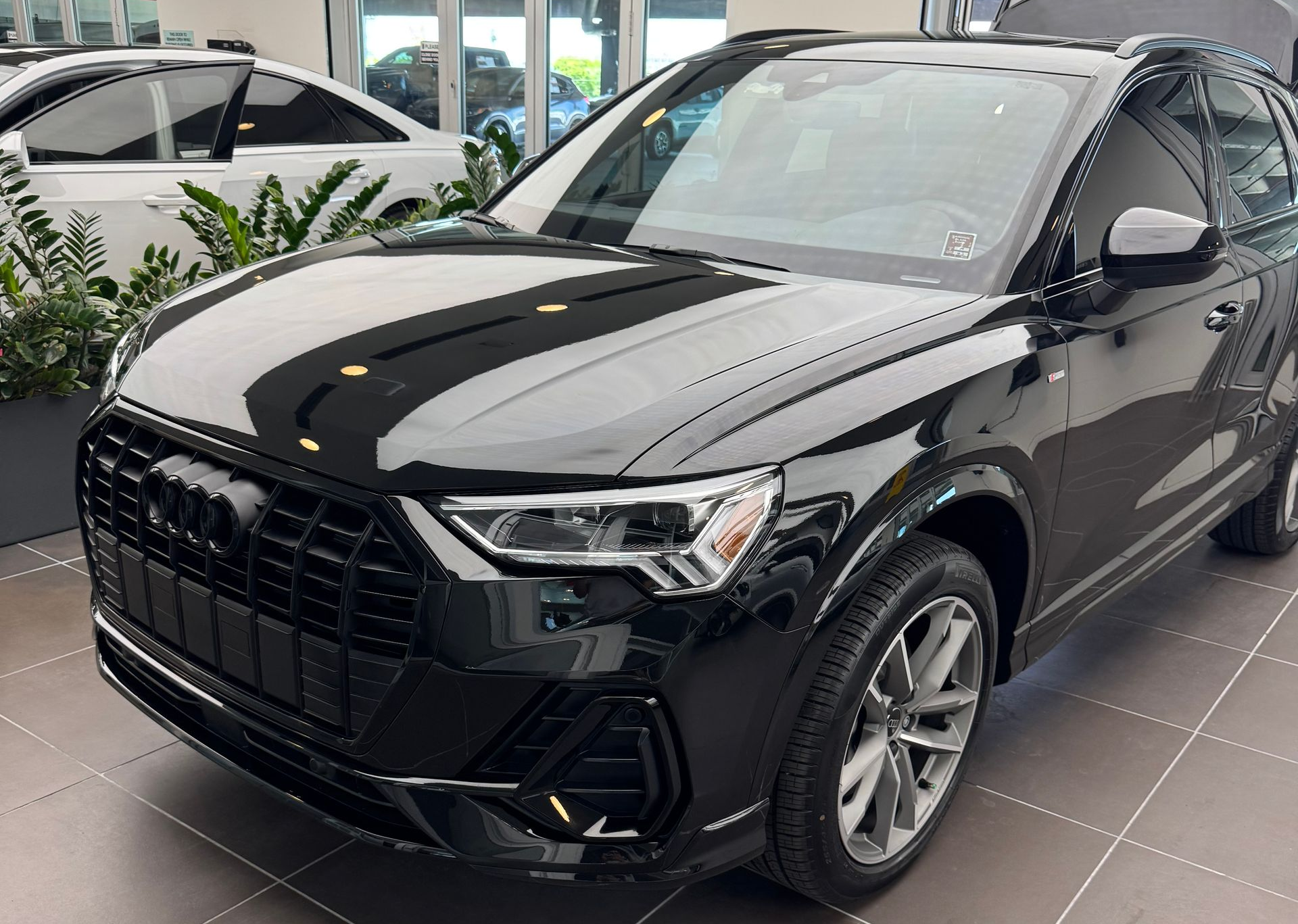 Black Audi Q3 SUV parked indoors, front view, shiny finish, silver wheels, in a dealership.