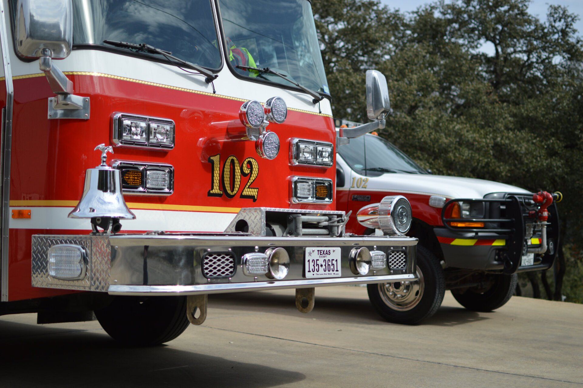 A red and white fire truck with the number 102 on the front is parked next to another fire truck