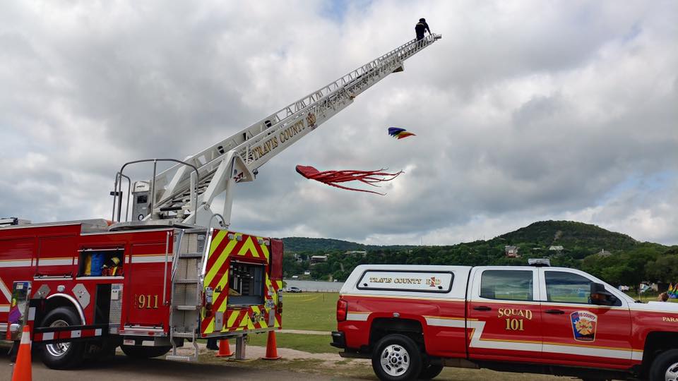A fire truck is parked next to a truck with a kite flying in the sky.