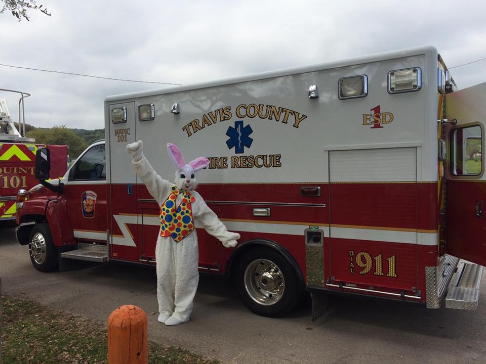 An Easter bunny mascot is standing in front of an ambulance.