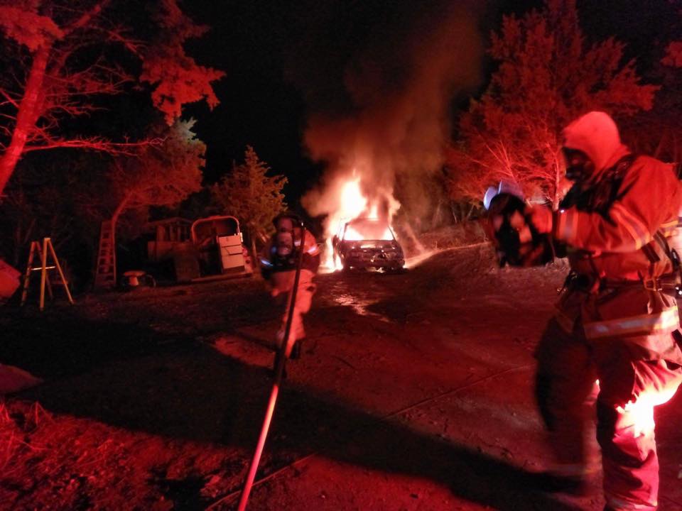 A fire fighter is standing in front of a car that is on fire.