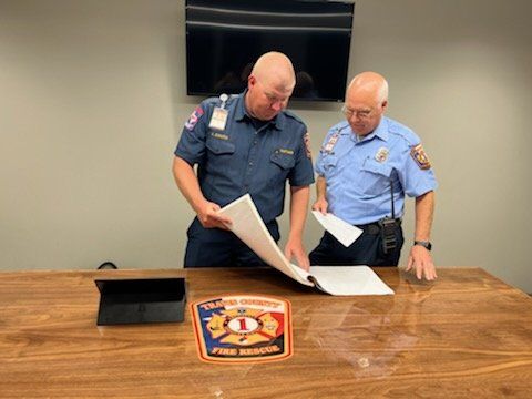 Two firefighters are looking at a piece of paper on a table.
