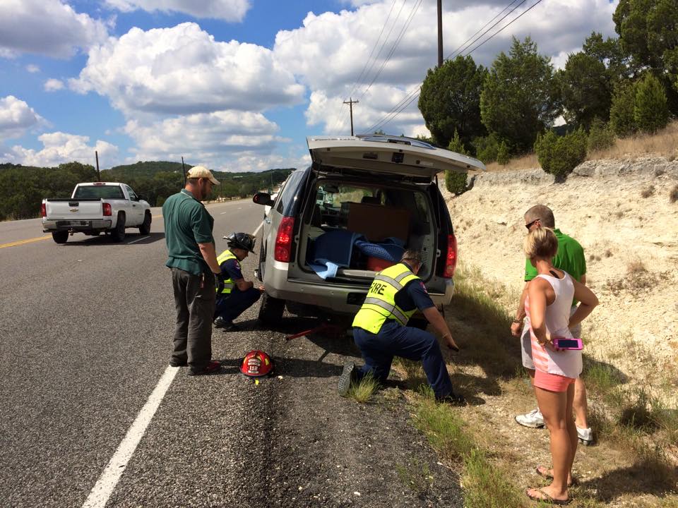 A group of people are standing on the side of a road next to a broken down car.