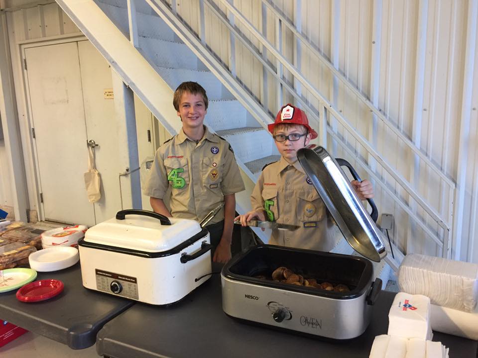 Two boy scouts are standing next to a table serving food.