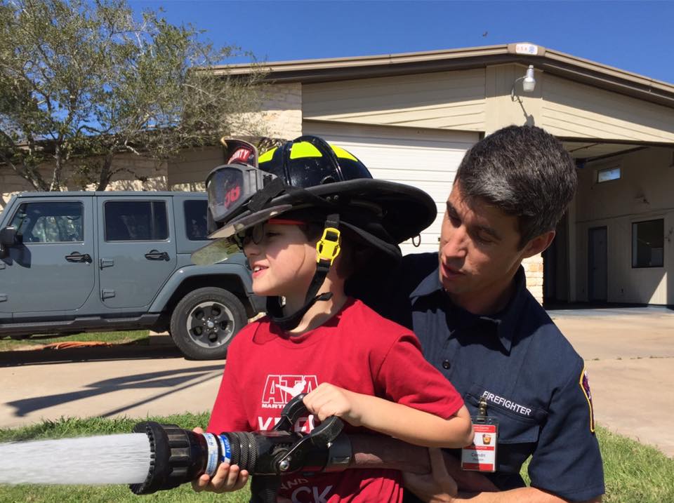 A fireman is helping a young boy with a fire hose.