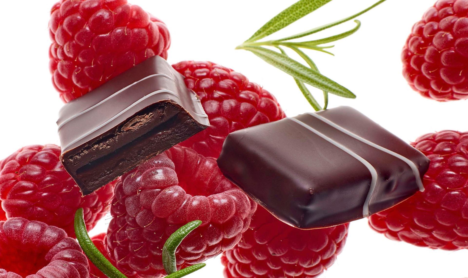 A chocolate bar is surrounded by raspberries and rosemary