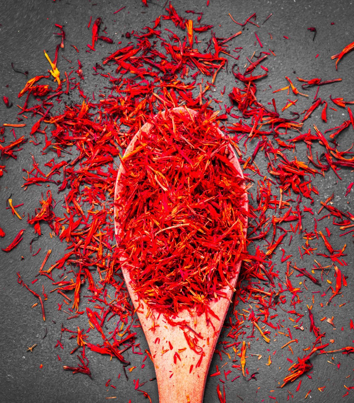 A wooden spoon filled with red saffron on a table.