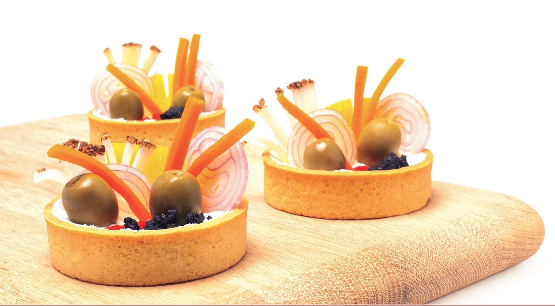 Three small tarts with olives and carrots on a cutting board
