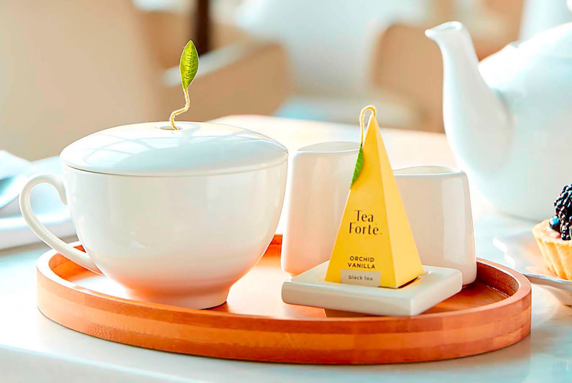 A cup of tea and a teapot are on a wooden tray on a table.