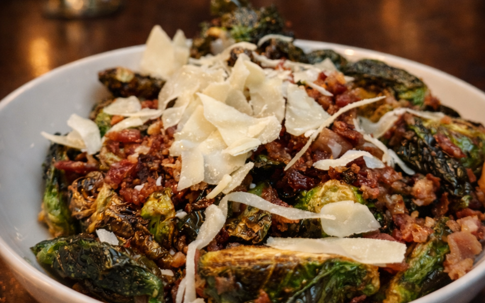 Roasted Brussels sprouts topped with shaved Parmesan and crispy breadcrumbs in a white bowl