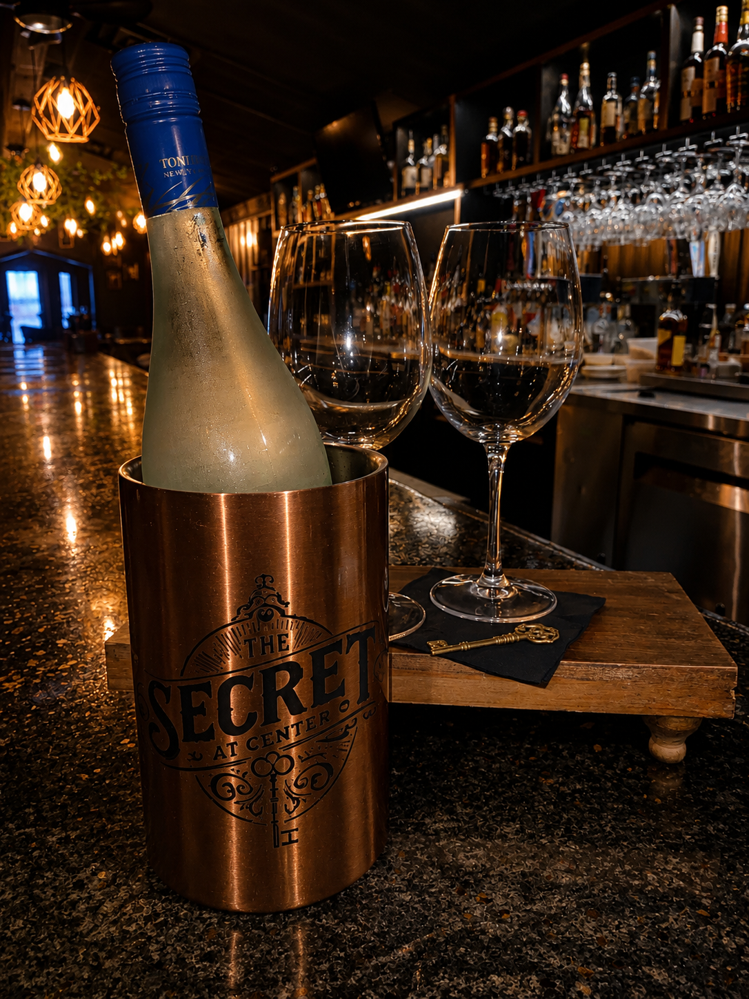 Bottle in a copper ice bucket on a bar counter with wine glasses and warm ambient lighting
