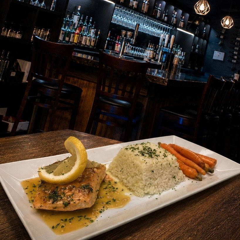 Pan-seared salmon with rice and carrots on a white plate in a dimly lit bar.