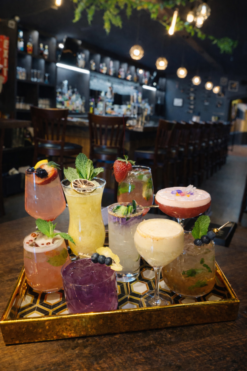 Assorted colorful cocktails on a tray at a dimly lit bar