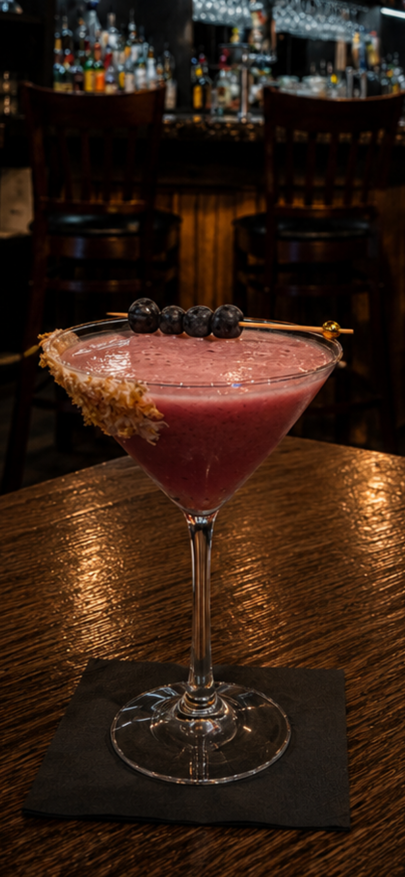 Pink cocktail in a martini glass with sugared rim and blackberries on a bar counter