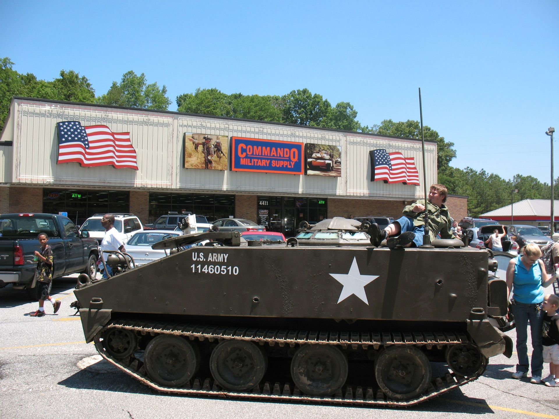 Tank in front of a military surplus store, American flags, people watching.