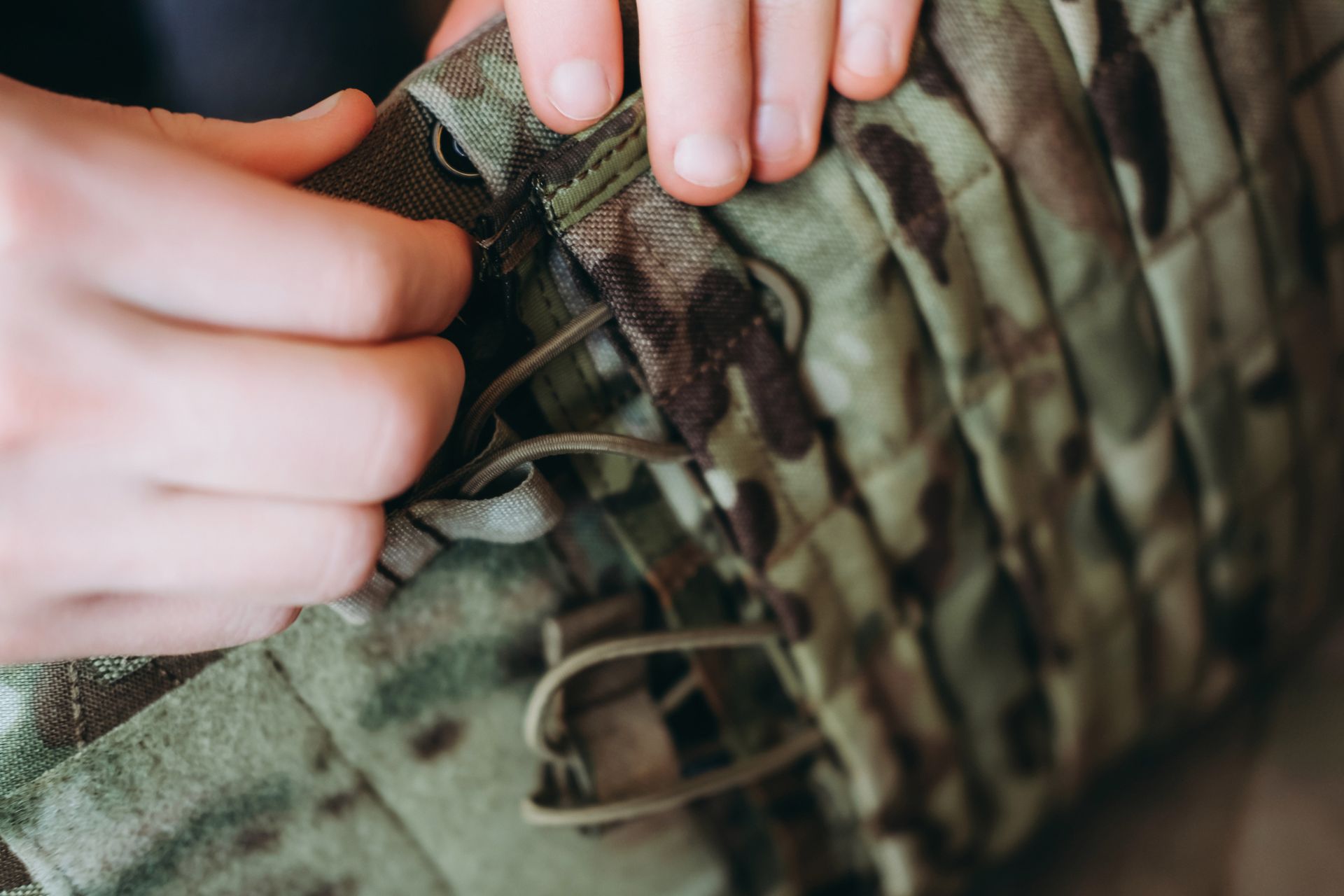 Hands adjusting straps on a camouflage tactical vest.