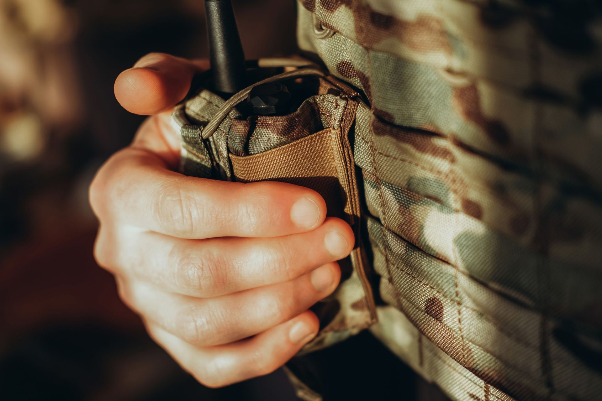 A person's hand holding a radio attached to a camouflage uniform.