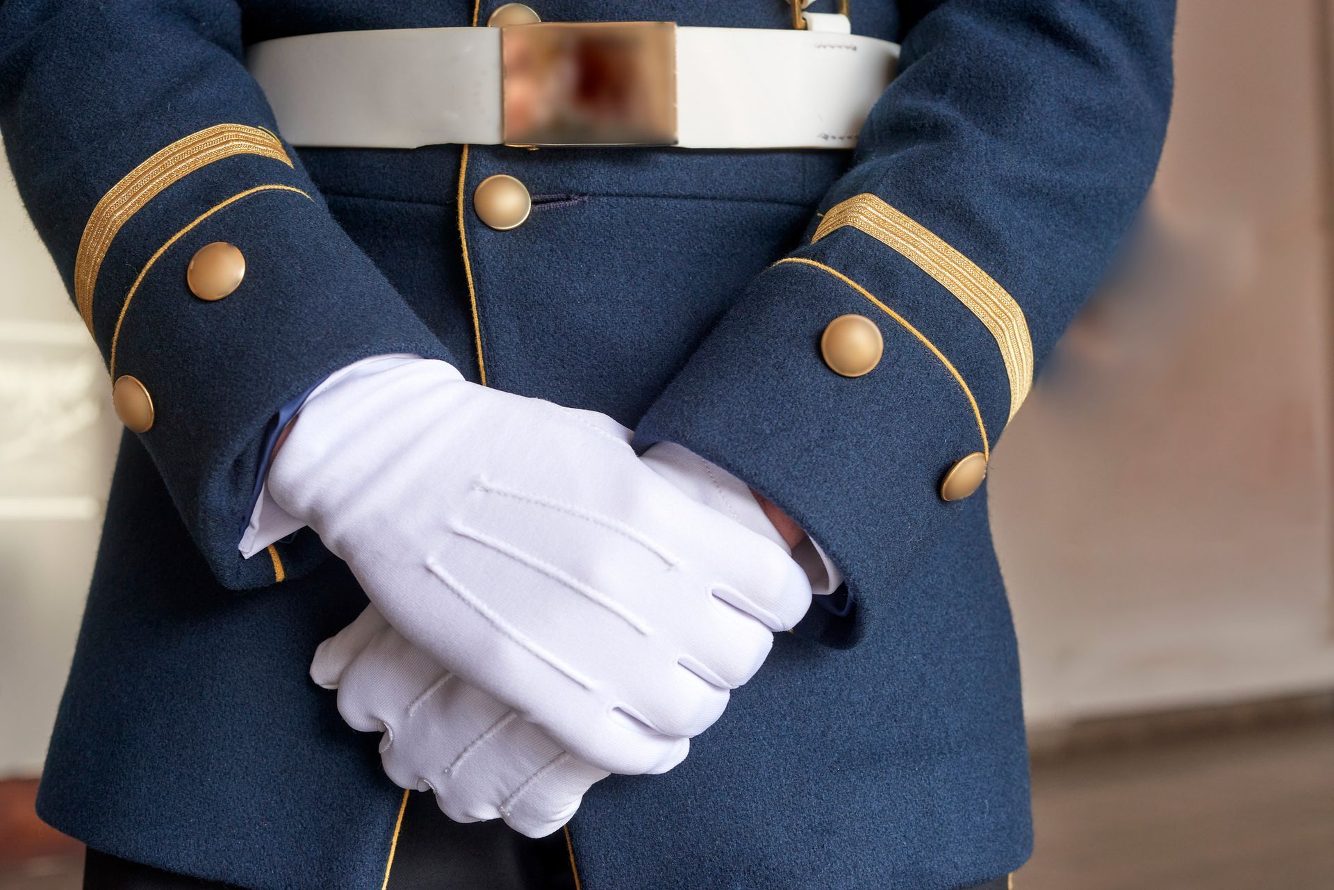 Person in blue uniform with white gloves, hands clasped at the waist.