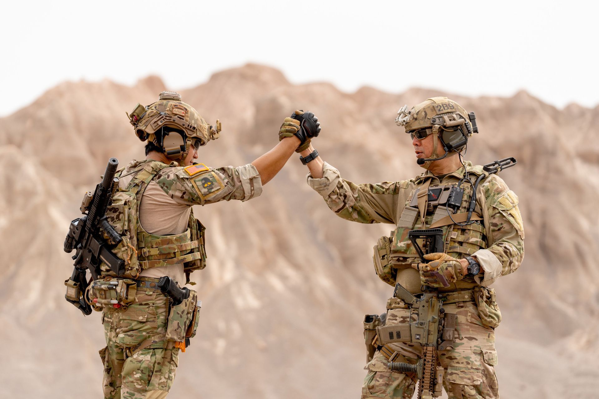 Two soldiers in camouflage gear high-five outdoors, desert background.