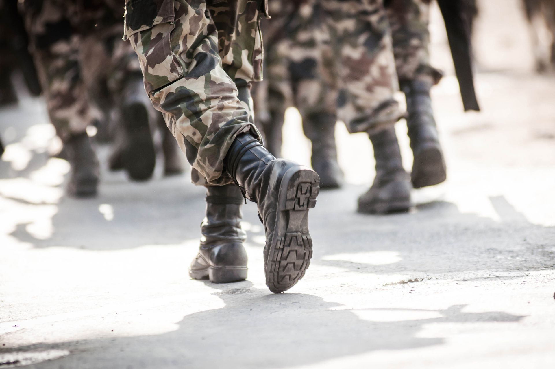 Soldiers in camouflage marching, viewed from the knees down, on a paved surface.