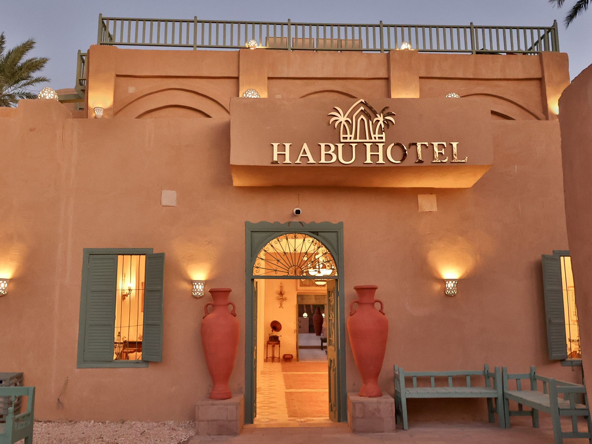 Habu Hotel entrance: beige building, arched doorway, large sign, teal accents, terracotta vases, exterior.