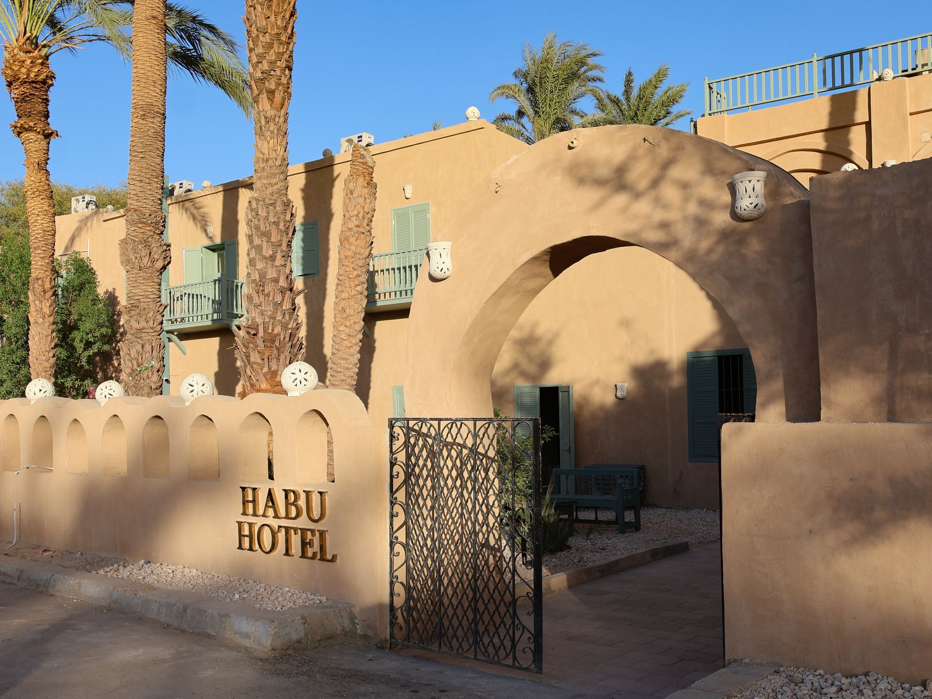 Habu Hotel entrance: arched doorway, beige stucco building, palm trees, iron gate, and 