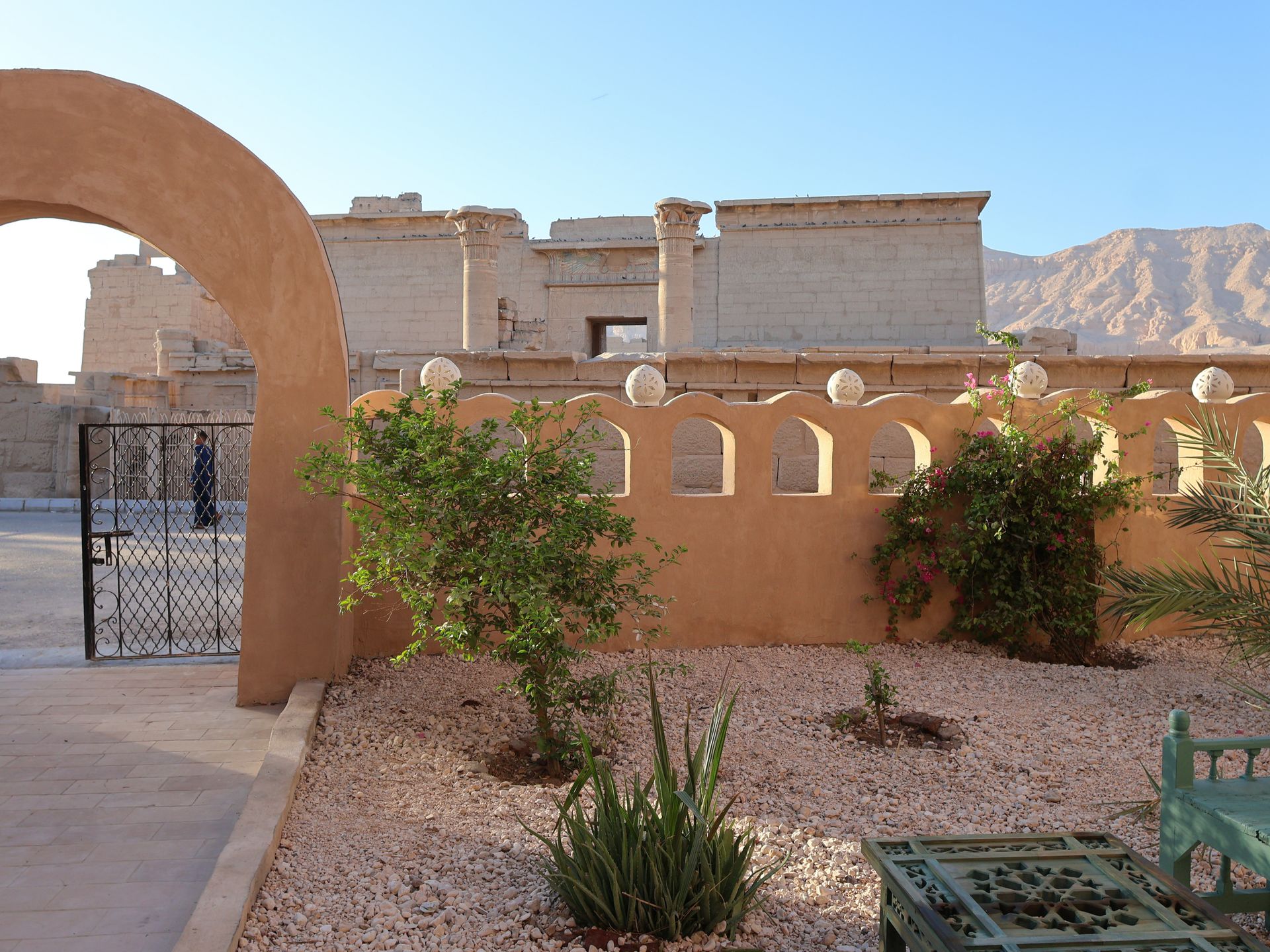 Courtyard with arched walls, plants, and view of ancient buildings and mountains.