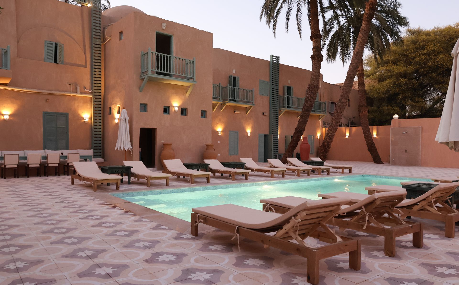 Poolside resort with lounge chairs, building with balconies, and palm trees.
