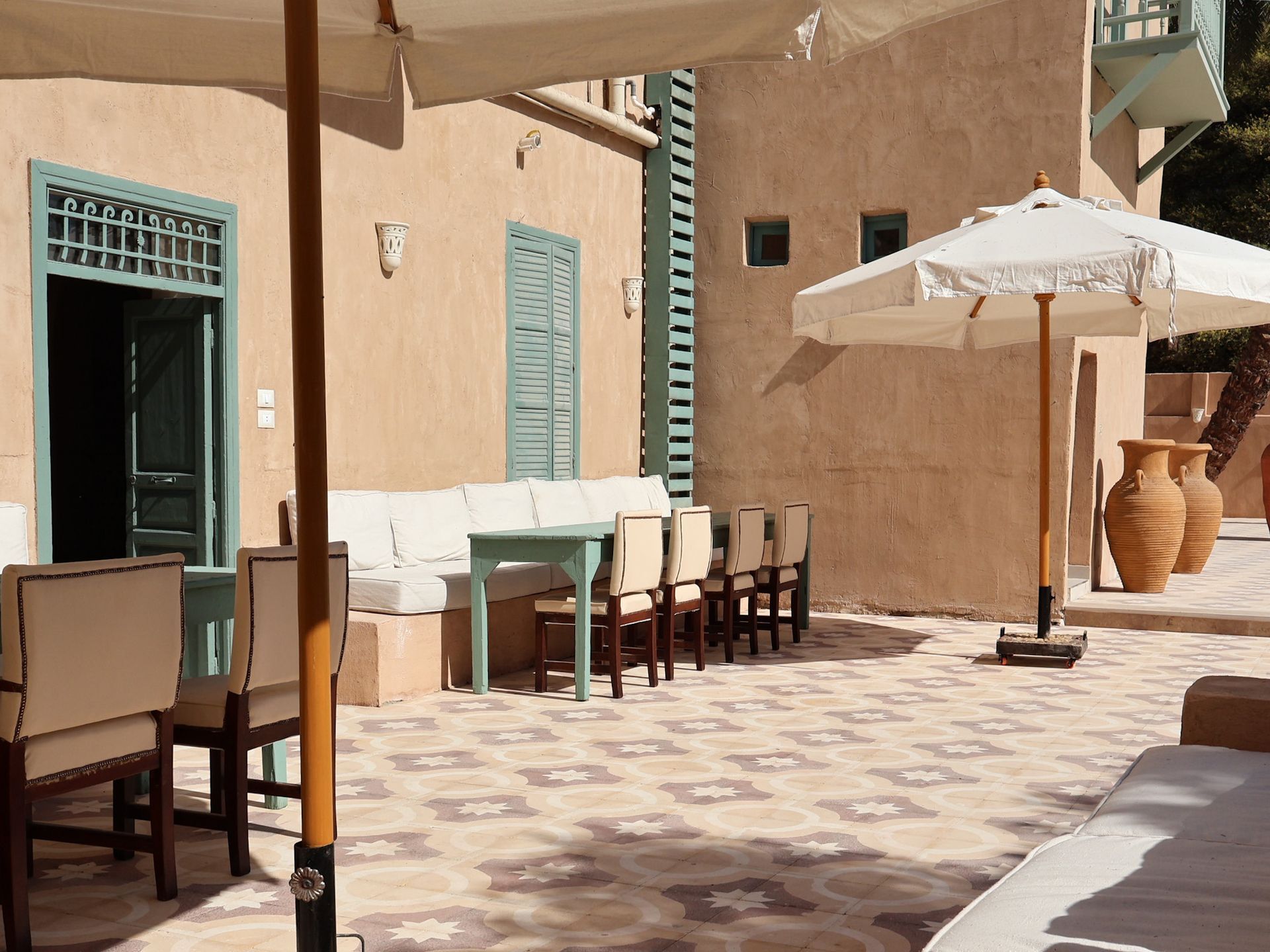 Courtyard with beige stucco walls, turquoise trim, tiled floor, white umbrellas, and seating.