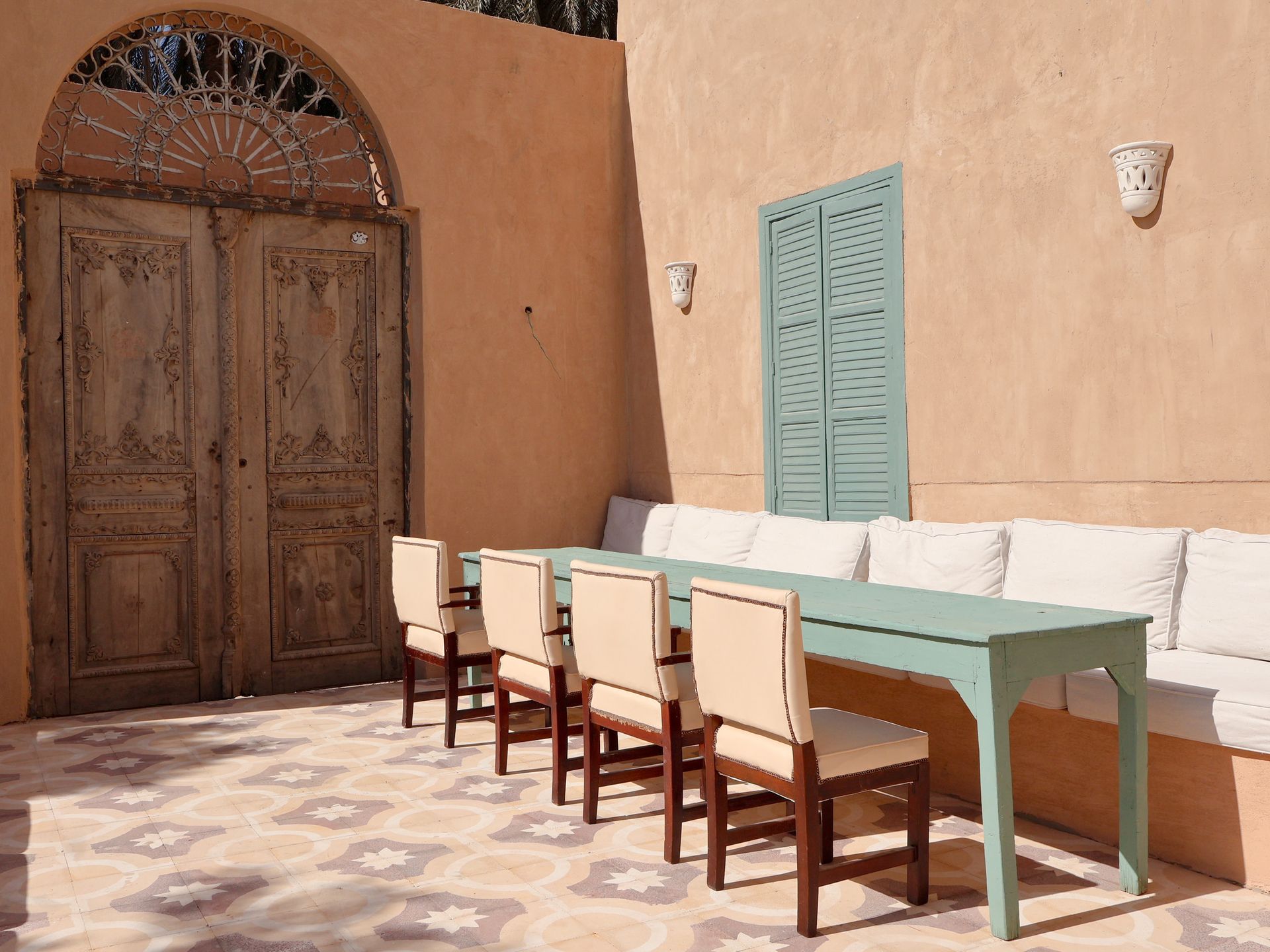 Outdoor dining area with a turquoise table, cream chairs, and a weathered wooden door.