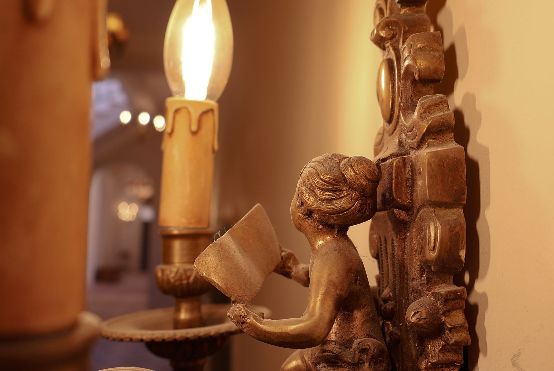 Bronze cherub reading a book next to a lit candle in a decorative sconce.