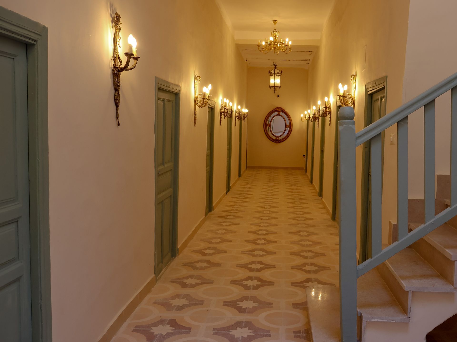 Long hallway with doors, sconces, and a staircase. Light-colored walls and patterned floor.