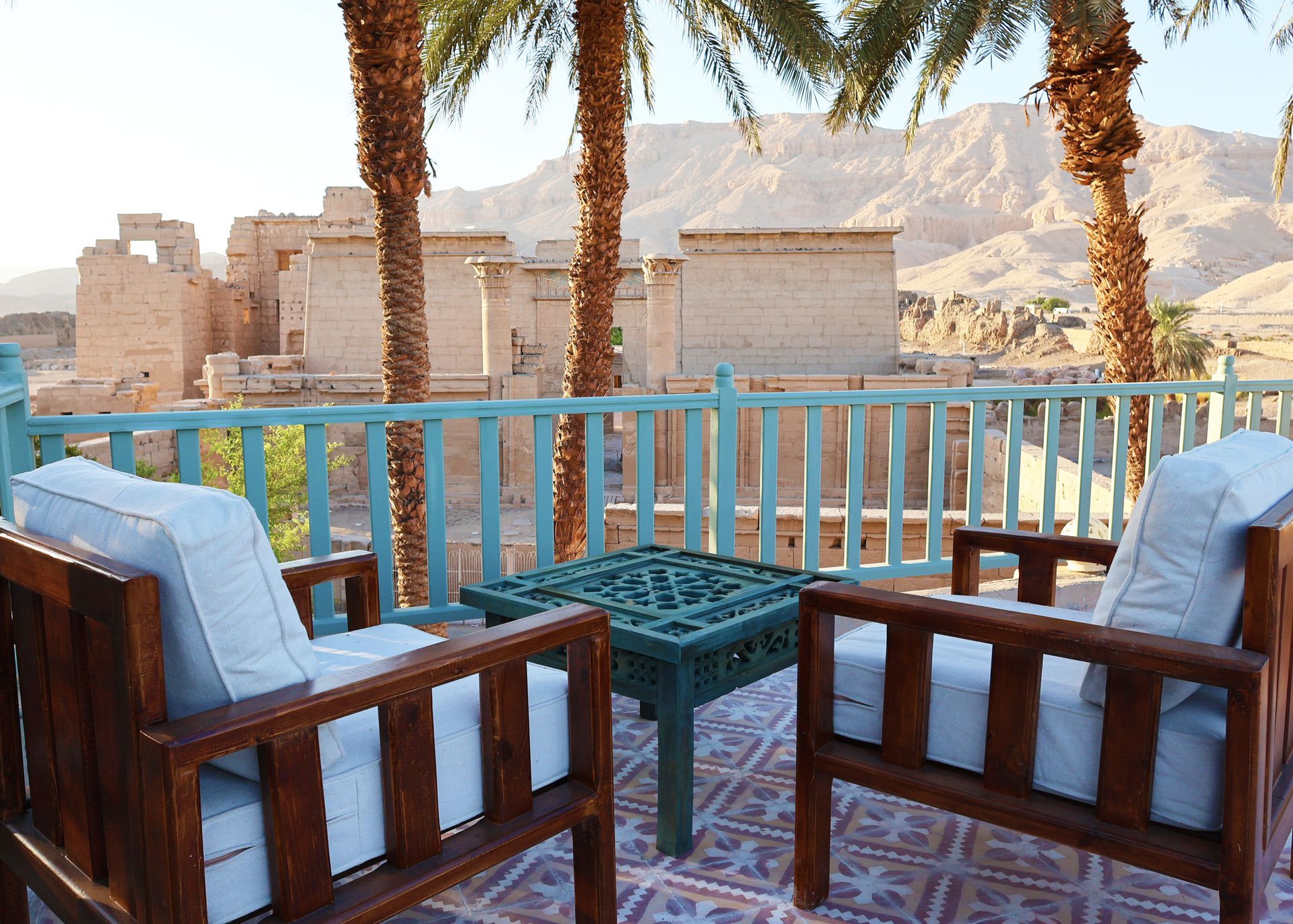 Outdoor seating overlooking ancient stone structures, palm trees, and mountains.