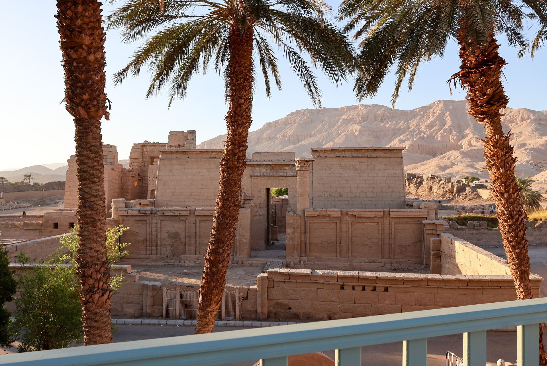 Ancient stone structure with palm trees, desert mountains in background.