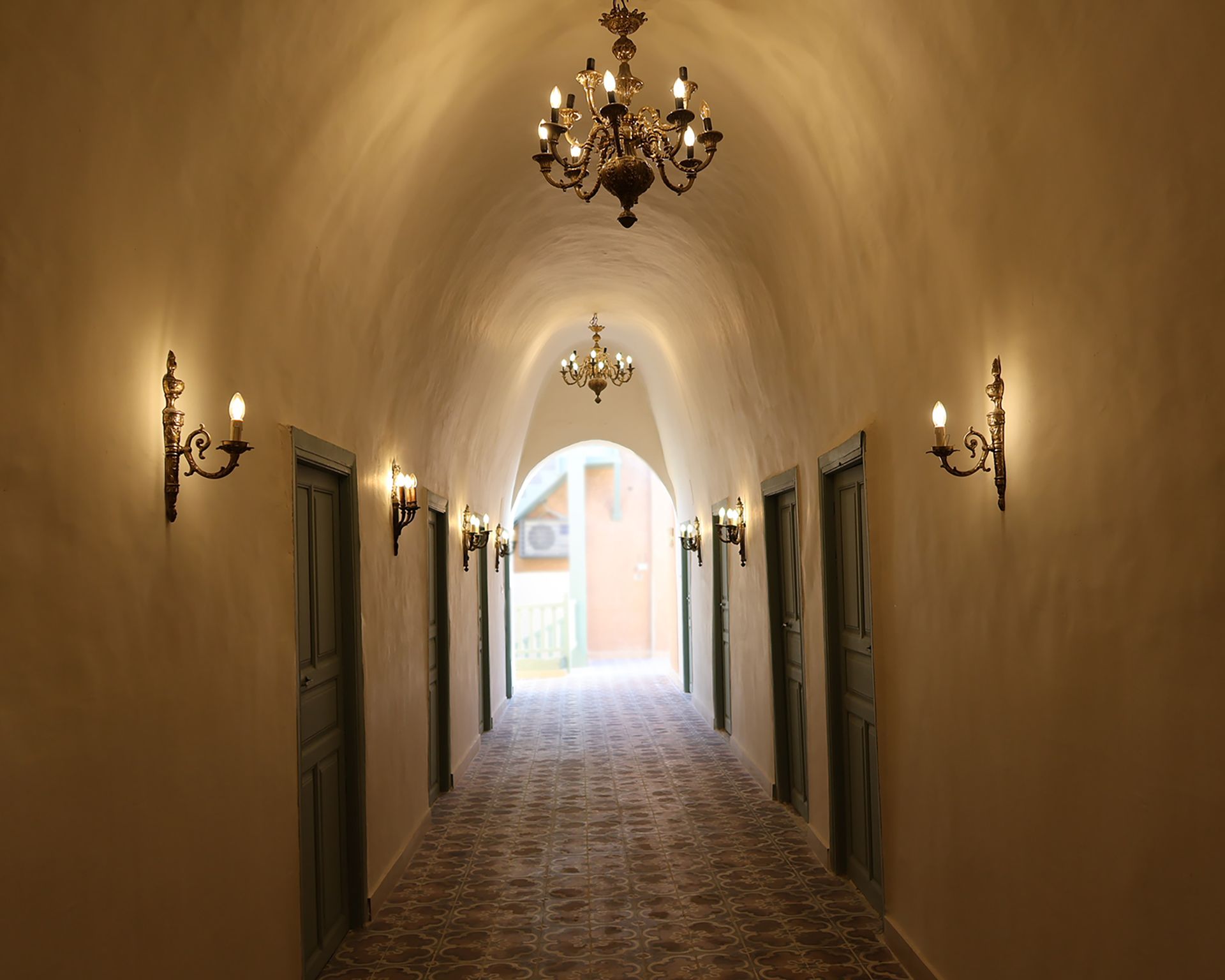 Long arched hallway with ornate chandeliers, sconces, and doors.