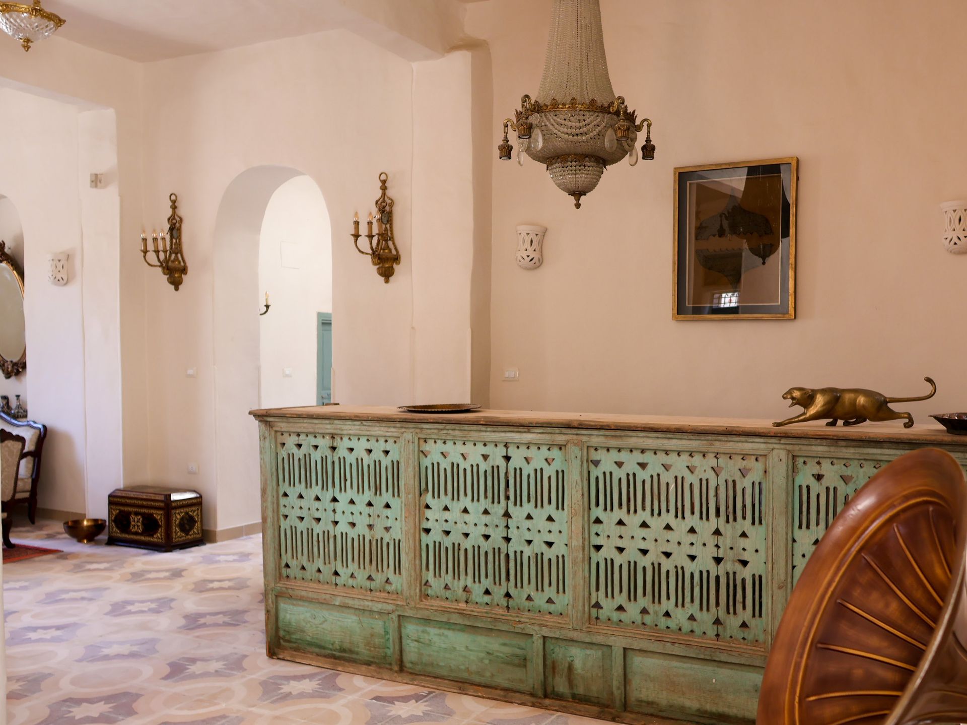 Reception desk in a building with carved teal panels and a gold chandelier.