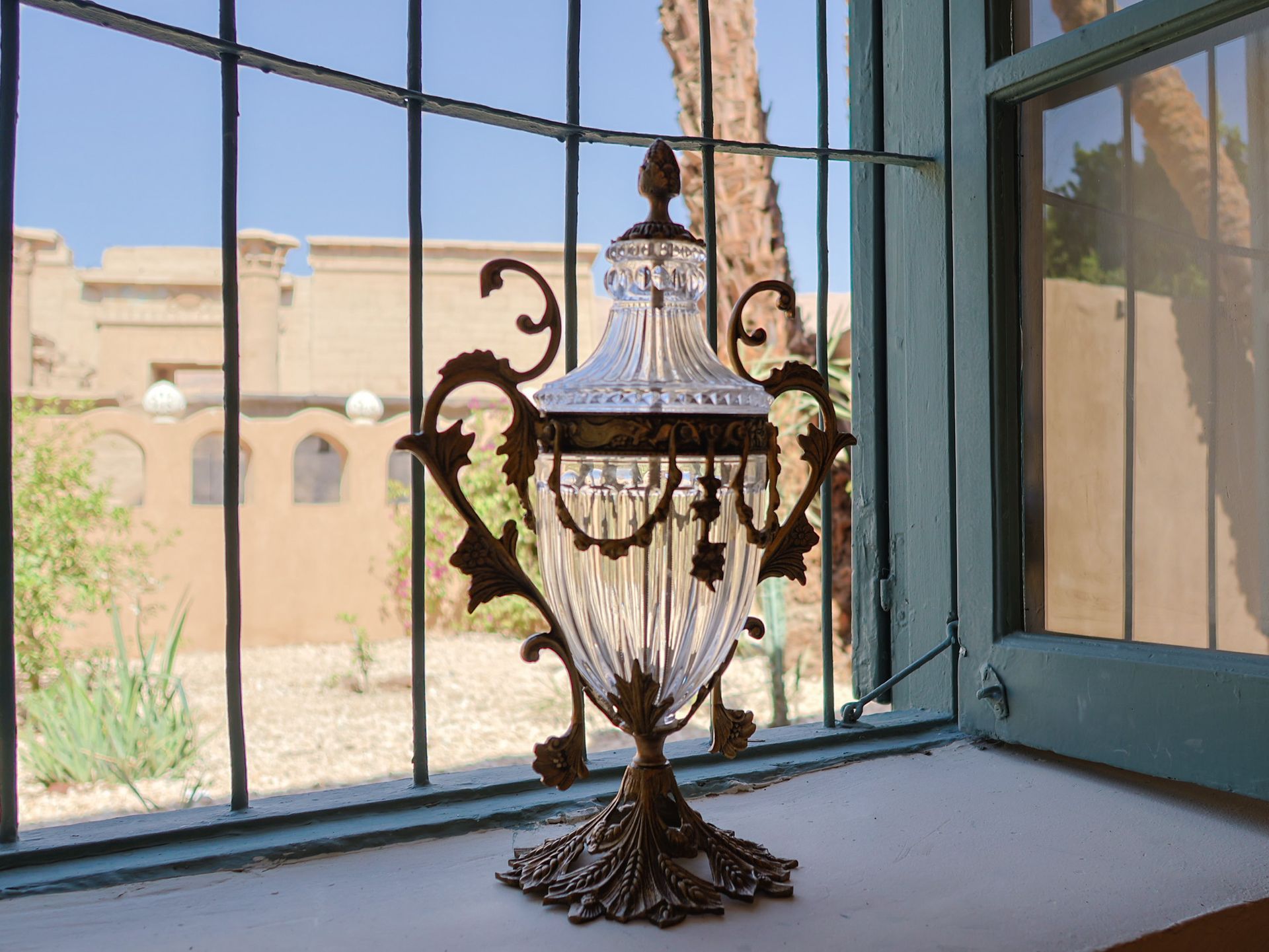 Ornate glass and metal vase on a windowsill, background of a building and sky.