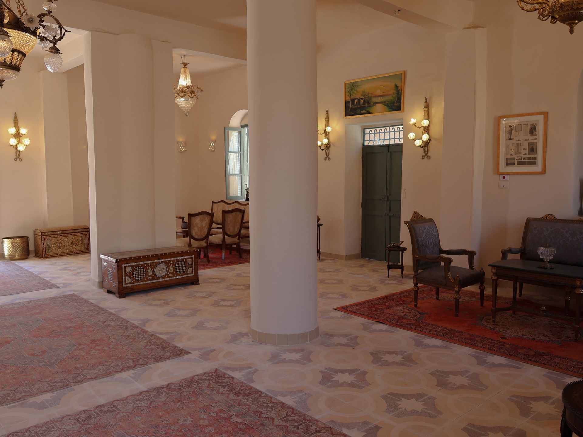 Elegant interior with columns, ornate rugs, chandeliers, and antique furniture.