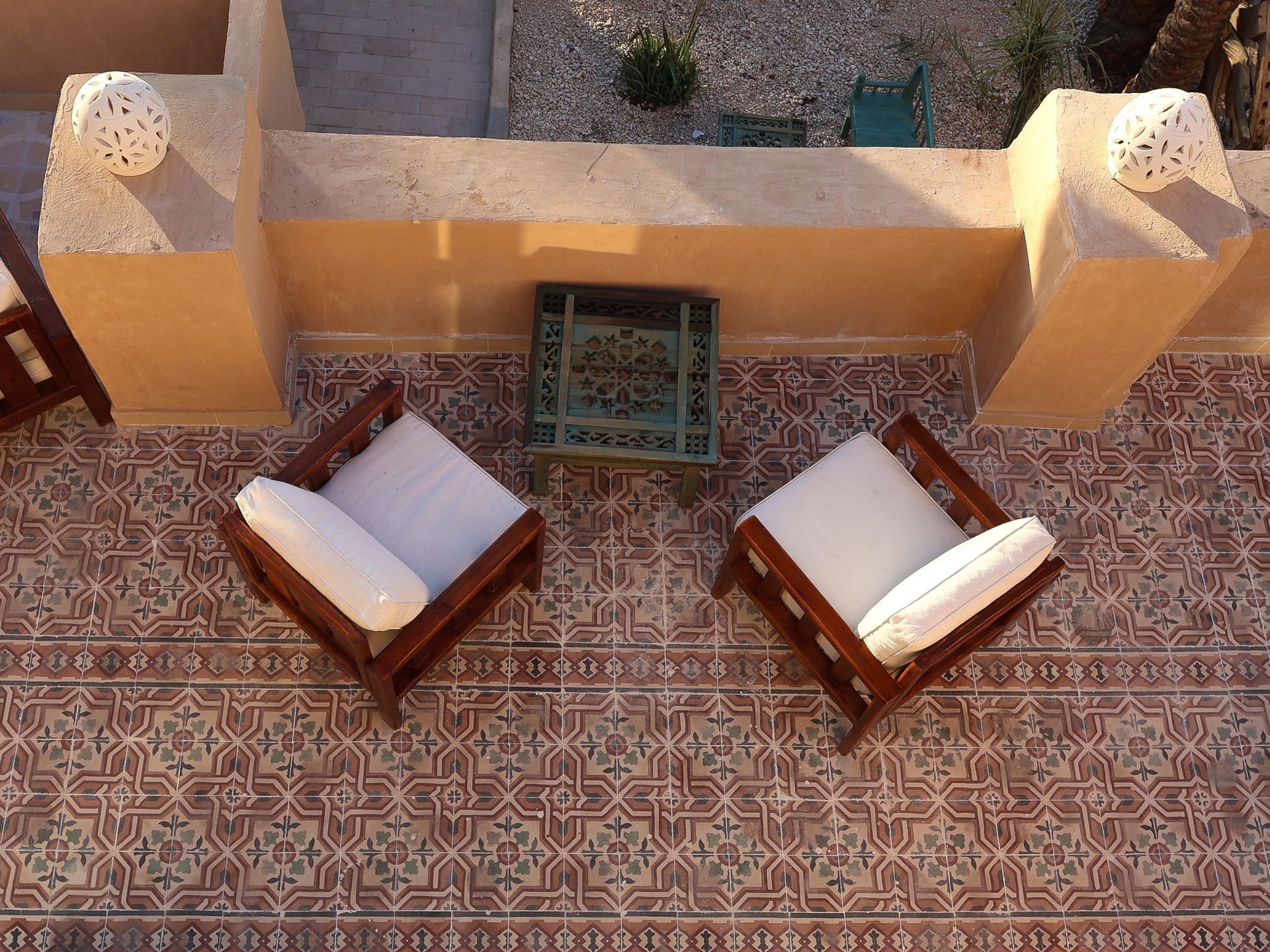 Two wooden chairs with white cushions and a small table on a tiled patio.