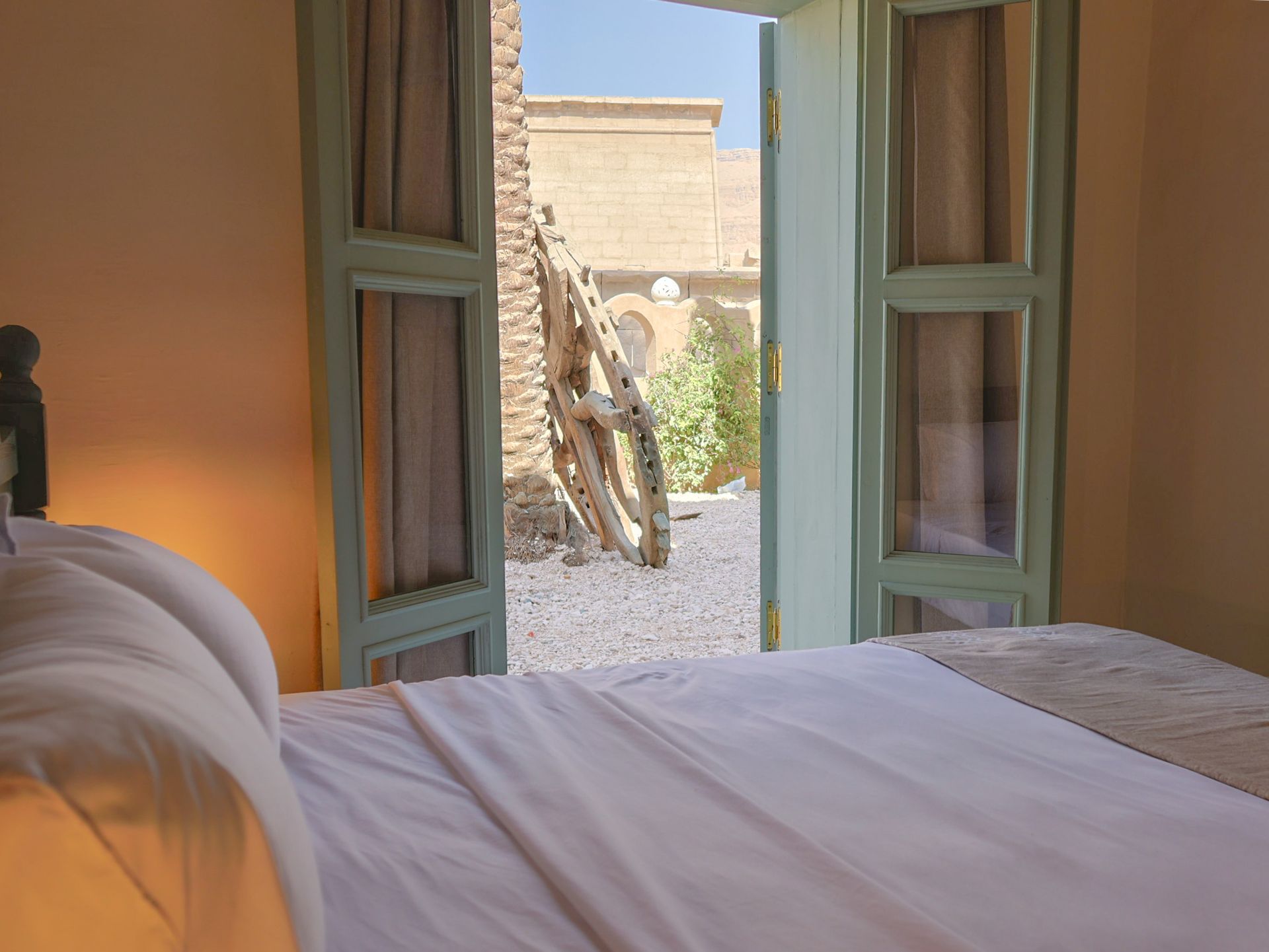 Bedroom with open turquoise door, leading to a small courtyard with gravel and a decorative wooden wheel.