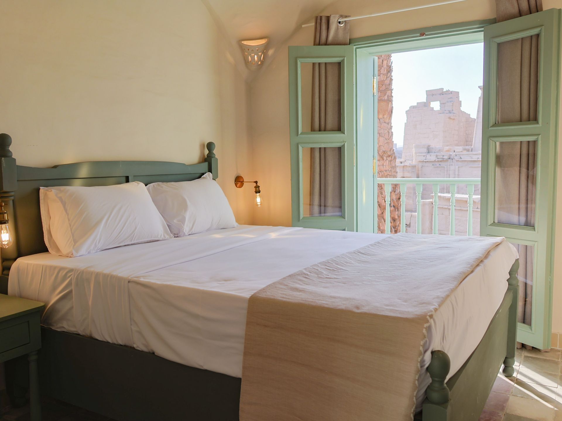 Bedroom with green bed frame and shutters, open doorway to cityscape.