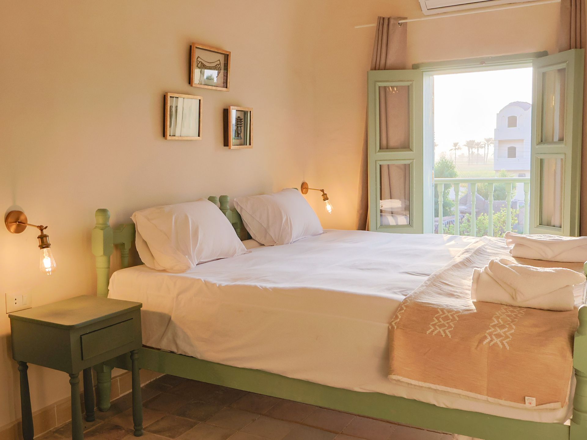 Bedroom with queen-sized bed, green trim, and open window. Includes nightstand, sconces, and artwork.