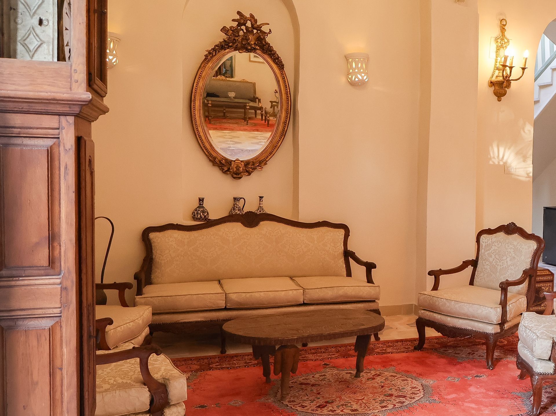 Living room with antique furniture, rug, large mirror, and grandfather clock.