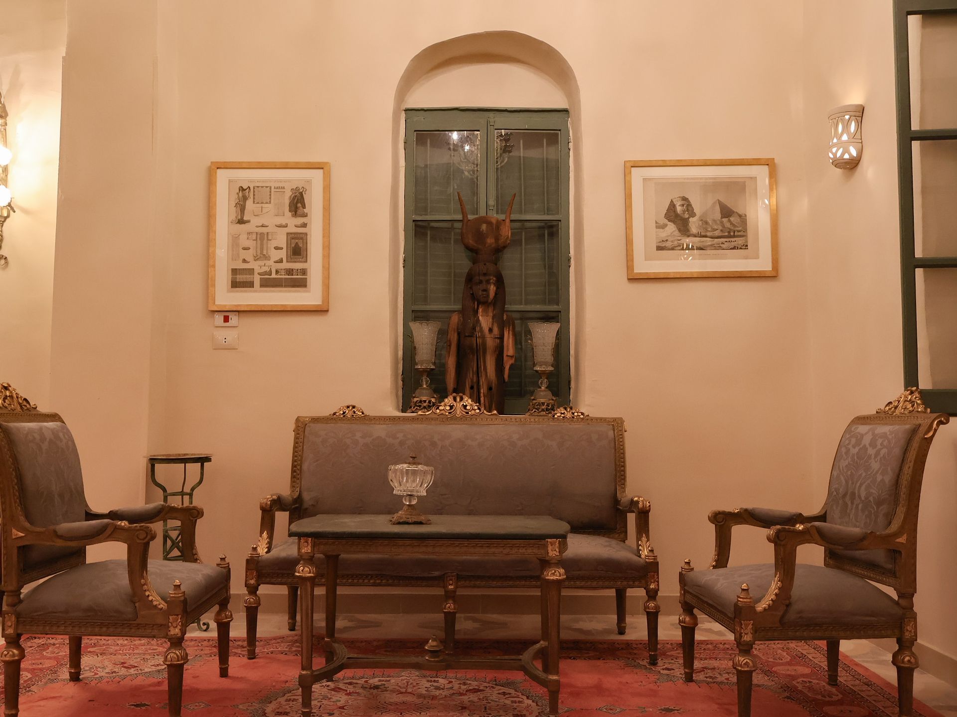 Living room with ornate furniture, artwork, and a statue in front of a window.